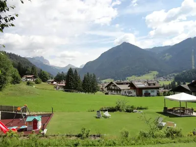 a large green field with mountains in the background at Appartamento Ciamp in Pozza di Fassa