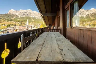a wooden table on a balcony with a view of mountains at Villa Allegra 2 Tofane monuntains view in Cortina dʼAmpezzo