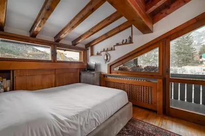 a bedroom with a bed in a room with windows at GuestHost - Cortina Charming Wooden Alpine Nest in Cortina dʼAmpezzo