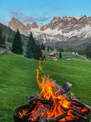 a fire in a pot in a field with mountains at Cesa Bernard - Apartment Cima 12 e new Apartment Fraine in Pozza di Fassa