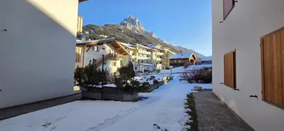 a snow covered street with buildings and a mountain at Casa Vaiolet in Pozza di Fassa