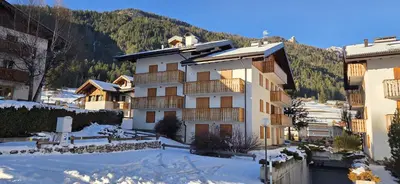 a large building in the snow with mountains in the background at Casa Vaiolet in Pozza di Fassa