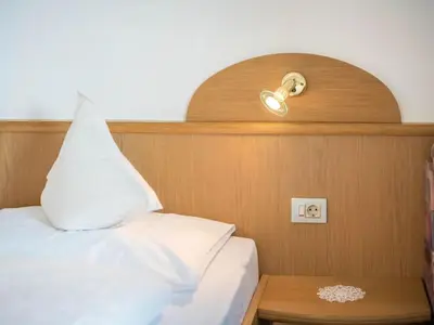 a bed with a white pillow and a light on a wall at Apartment Morgensonne by Interhome in Maranza