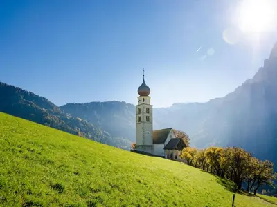a church on a green hill with the sun behind it at Apartment Wohnung in den Dolomiten mit traumhafter Aussicht by Interhome in Kastelruth