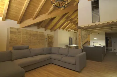 a living room with a couch and a kitchen at Sky Loft at Cervo - Panoramic Penthouse in Moena in Moena