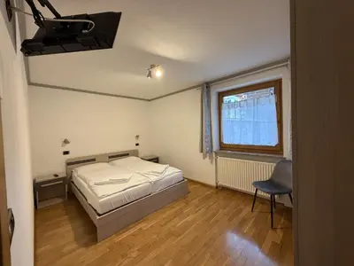 a bedroom with a bed and a chair and a window at Appartamento Star Begn - Piano Terra in Soraga