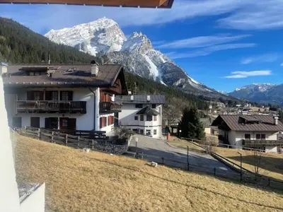 a house in a field with mountains in the background at Chalet Luxury Pelmo in San Vito di Cadore