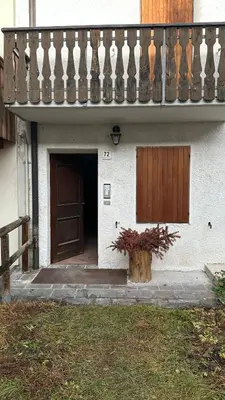 a building with a balcony and a door and a tree stump at HouSmart della Difesa 72 in San Vito di Cadore