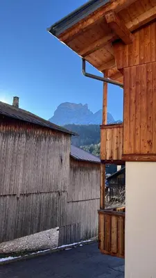 a barn with a wooden building with mountains in the background at HouSmart della Difesa 72 in San Vito di Cadore