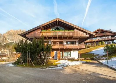an old building in a field with mountains in the background at Cianderies Cozy Apartment R&R in Cortina dʼAmpezzo