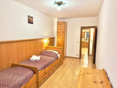 a room with two beds and a wooden table at Casa Cortina 3 camere da letto e parcheggio in Cortina dʼAmpezzo