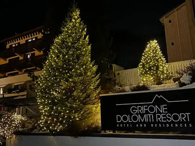 three christmas trees with lights in front of a sign at Grifone Dolomiti Residences in Arabba