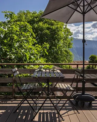 a table and chair with an umbrella on a deck at Mountain View Suites in Tesimo