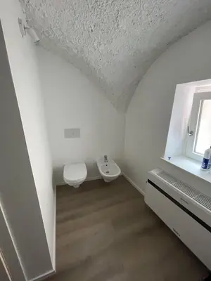 a white bathroom with a toilet and a window at Casetta in centro storico in Bedollo