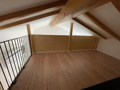 an attic room with a wooden floor and wooden beams at Casetta in centro storico in Bedollo