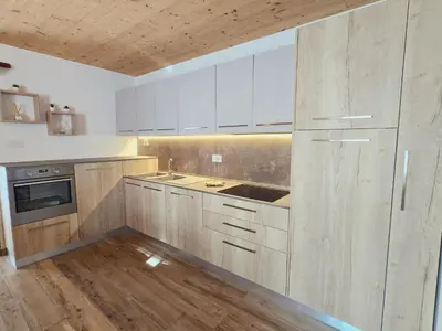 a kitchen with white cabinets and a wooden floor at La Perla di Fassa - Alpine Stay Apartments in Moena