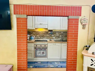 a kitchen with white cabinets and a red brick wall at Trilli House in Rocca Pietore