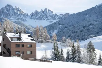 a house on a snowy hill with mountains in the background at Trutscher Häusl in Villnöss - Chalet in den Dolomiten mit Blick auf die Geisler in Funes
