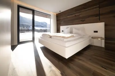 a bedroom with a white bed and a large window at Trutscher Häusl in Villnöss - Chalet in den Dolomiten mit Blick auf die Geisler in Funes