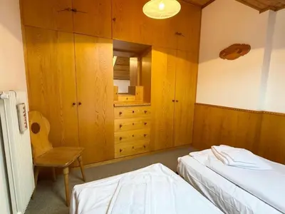 a bedroom with two beds and a chair and cabinets at Apartment Roacia-5 by Interhome in Alba di Canazei