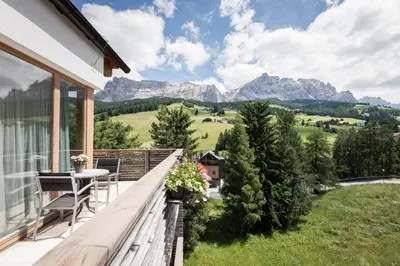 a balcony with a table and chairs and mountains at Alpine Hotel Ciasa Lara in La Villa