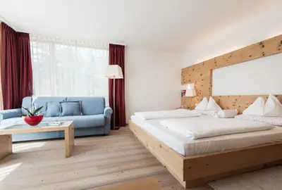 a bedroom with a large bed and a blue couch at Alpine Hotel Ciasa Lara in La Villa