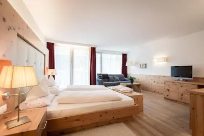 a bedroom with a bed and a couch and a television at Alpine Hotel Ciasa Lara in La Villa