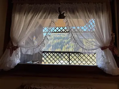 a window with white curtains and a view of trees at Red Alpine Olympic Apartment near Cortina in San Vito di Cadore