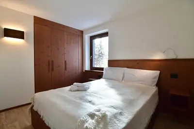 a bedroom with a bed with white sheets and a window at Mazzantini appartamento vacanza San Martino di Castrozza in San Martino di Castrozza