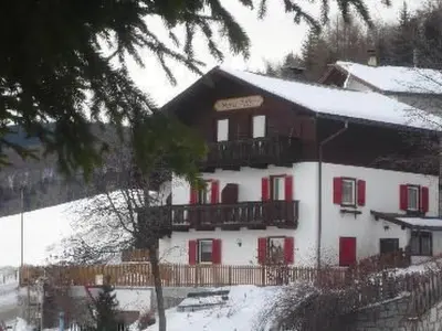a large building with red shuttered windows and snow at Apartment Haus Adler by Interhome in Maranza