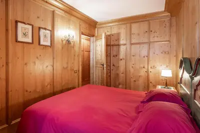 a bedroom with wooden walls and a bed with a pink bedspread at Cozy basement flat just few steps from centre in Cortina dʼAmpezzo