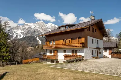 a large wooden house with mountains in the background at Cozy basement flat just few steps from centre in Cortina dʼAmpezzo