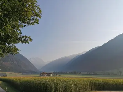 a field with a house and mountains in the background at Branterhof in Rasun di Sopra