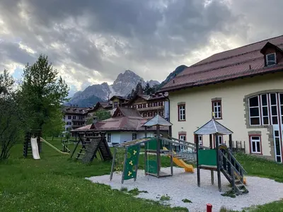 a playground in front of a building with mountains in the background at Villaggio Ploner in Dobbiaco