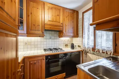 a kitchen with wooden cabinets and a black dishwasher at Cozy 3 bedroom with beautiful view and access to garden in Cortina dʼAmpezzo