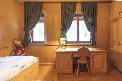 a bedroom with a bed and a desk with a window at Casa Merisanda, confortevole e immersa nel verde in Cortina dʼAmpezzo