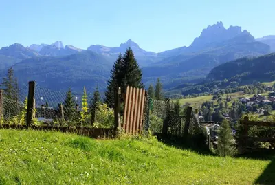 a fence on a hill with mountains in the background at Brand new beautiful ground floor flat in Cortina dʼAmpezzo