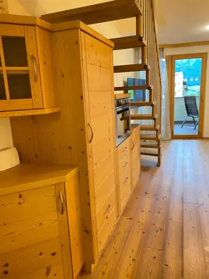 a kitchen with wooden cabinets and a spiral staircase at dolomites view apartment 2 in Rasun di Sopra