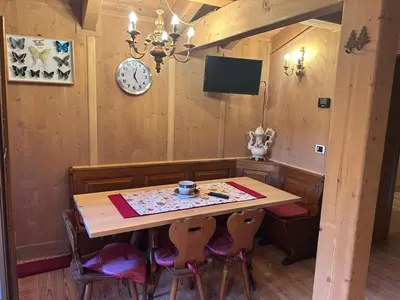 a dining room table with chairs and a clock on the wall at Appartamento cozy tra le montagne in San Vito di Cadore