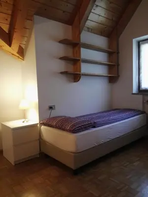 a bedroom with a bed and a shelf on the wall at Casa Sergio in Ziano di Fiemme