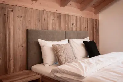 a bed with white pillows in a room with wooden walls at Deluxe Apartments Lantl in Falzes