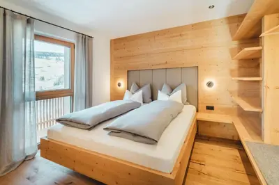 a bedroom with a large bed with a wooden wall at Kuenzerhof Apartments in Braies