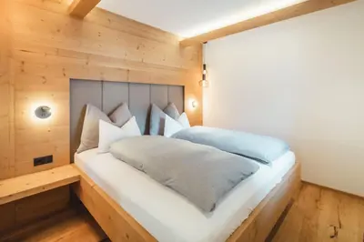 a bedroom with a white bed with wooden walls at Kuenzerhof Apartments in Braies