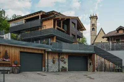 a house with a balcony on top of it with a clock tower at Family-Friendly Mountain Home In The Dolomites in Campitello di Fassa