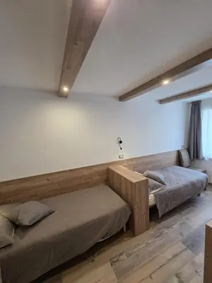 two beds in a room with white walls and wooden floors at Appartamento La Meridiana in Tonadico