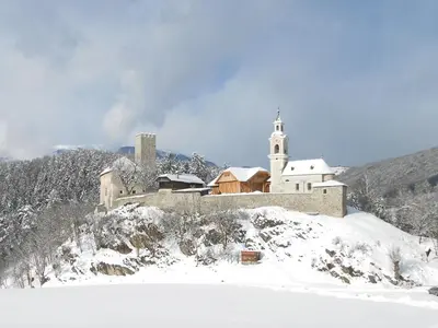 a building on top of a snowy hill with a church at Ferienwohnung Lamprechtsburg in Brunico