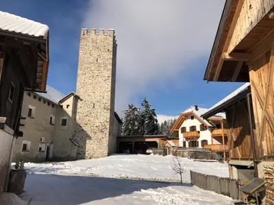a building with a tall tower in the snow at Ferienwohnung Lamprechtsburg in Brunico