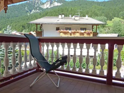 a chair on a balcony with a view of a house at Appartamenti Majon Sotroi in Campitello di Fassa