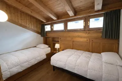 two beds in a room with wooden walls and windows at Alverà Apartment in Cortina dʼAmpezzo