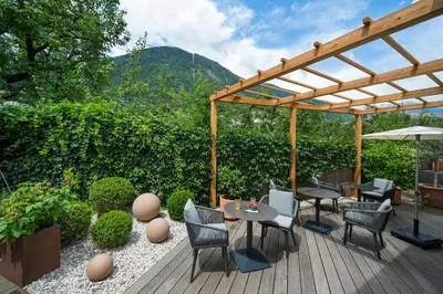 a patio with chairs and tables and a wooden pergola at Hotel Jardis in Lana